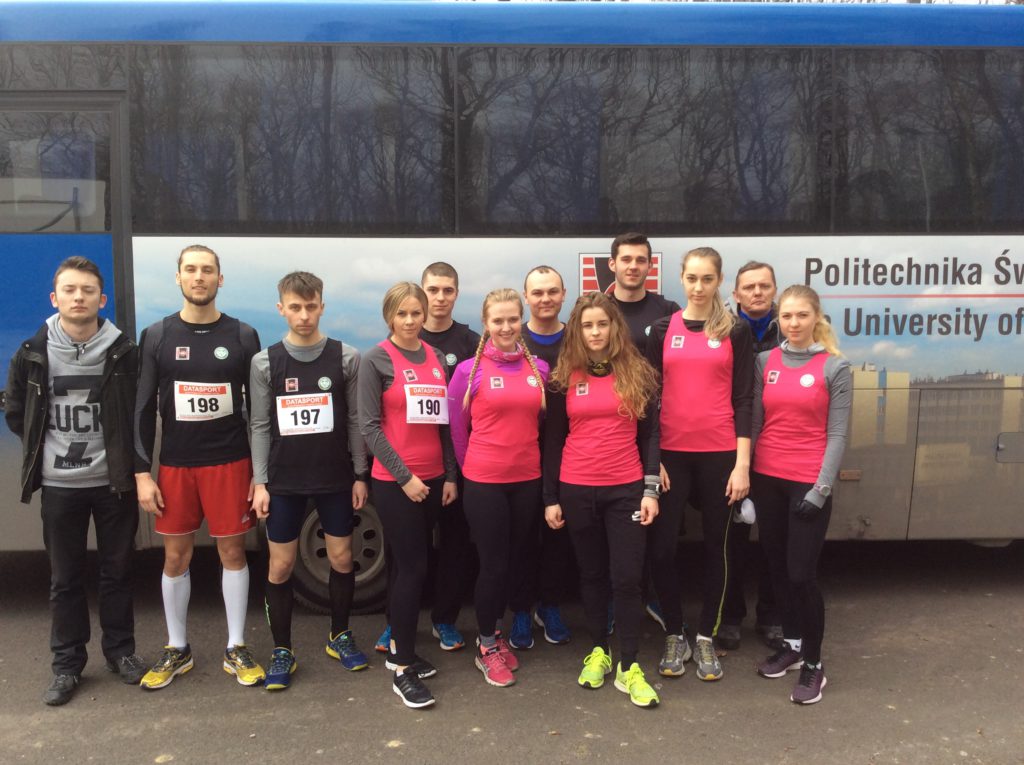 Grupa ludzi w strojach sportowych stoi przed autobusem z napisem 