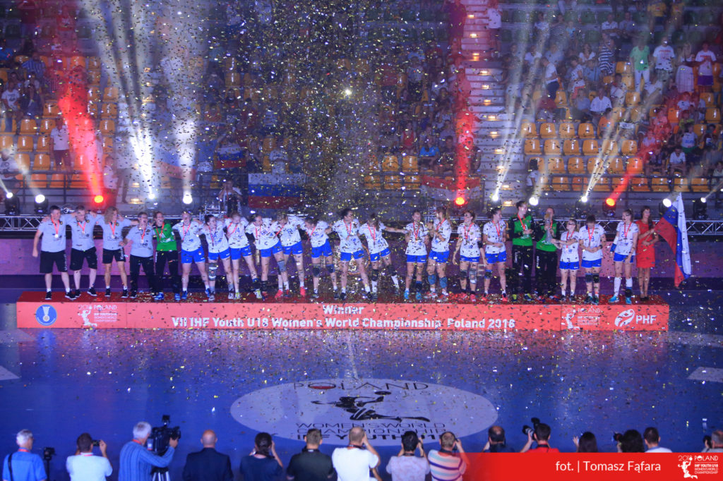 Drużyna piłki ręcznej świętuje zwycięstwo na podium, obsypana konfetti.