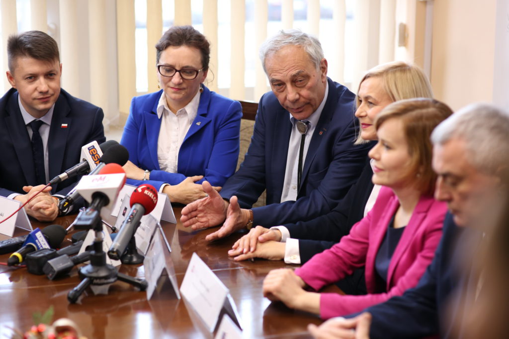 Ludzie przy stole z mikrofonami. Konferencja prasowa.