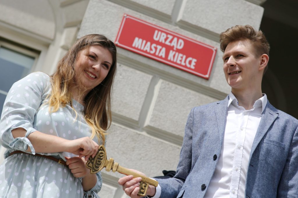 Młoda kobieta i mężczyzna trzymają złoty klucz przed budynkiem z napisem 