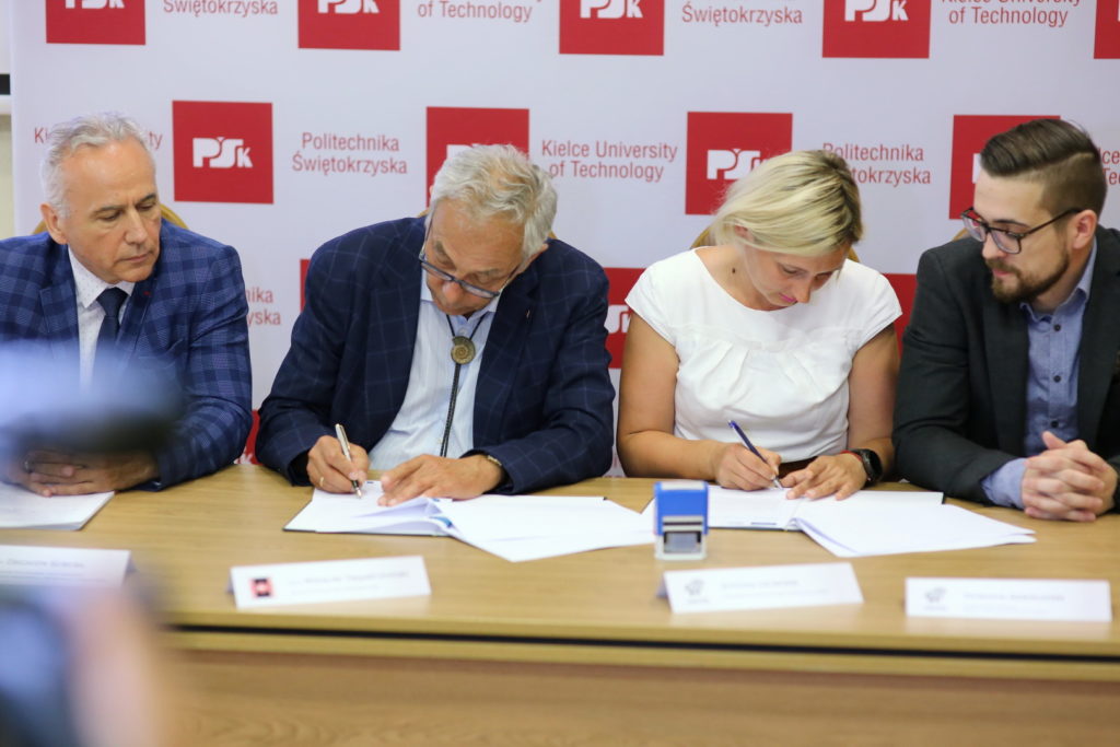 Cztery osoby siedzą przy stole, podpisując dokumenty. W tle widnieje logo Politechniki Świętokrzyskiej.