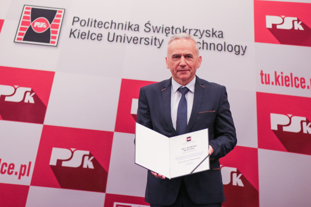 Mężczyzna w garniturze trzyma dokument. W tle logo Politechniki Świętokrzyskiej.