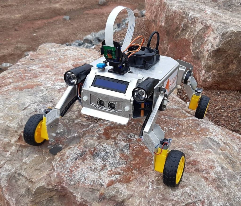 Sześciokołowy robot z kamerą i czujnikami na kamienistym podłożu.