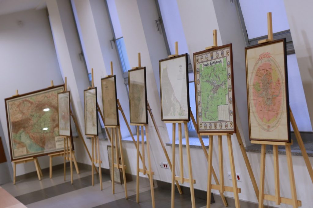 Wystawa starych map na sztalugach. Widoczne mapy Krakowa, Katowic i innych regionów.