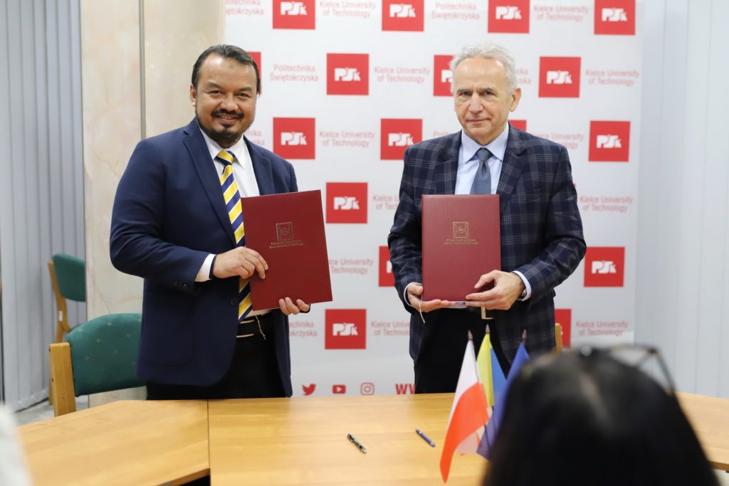 Dwóch mężczyzn w garniturach trzyma czerwone teczki. W tle logo Politechniki Świętokrzyskiej.