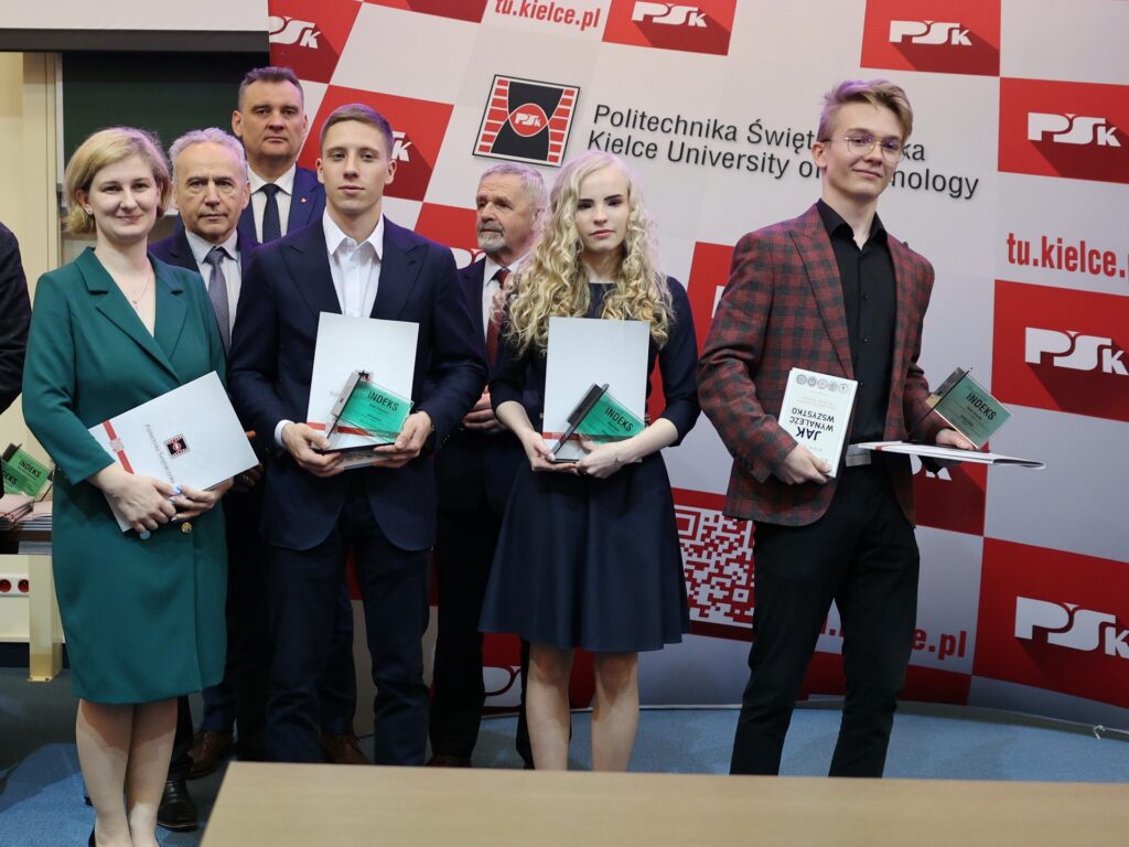 Osoby odbierają nagrody na tle logo Politechniki Świętokrzyskiej. Kluczowe obiekty: ludzie, nagrody, dokumenty.