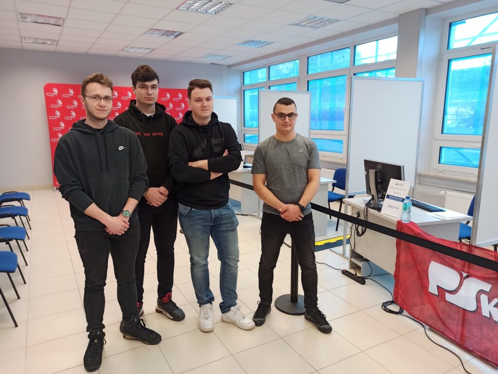 Czterech młodych mężczyzn stoi w pomieszczeniu z banerem 