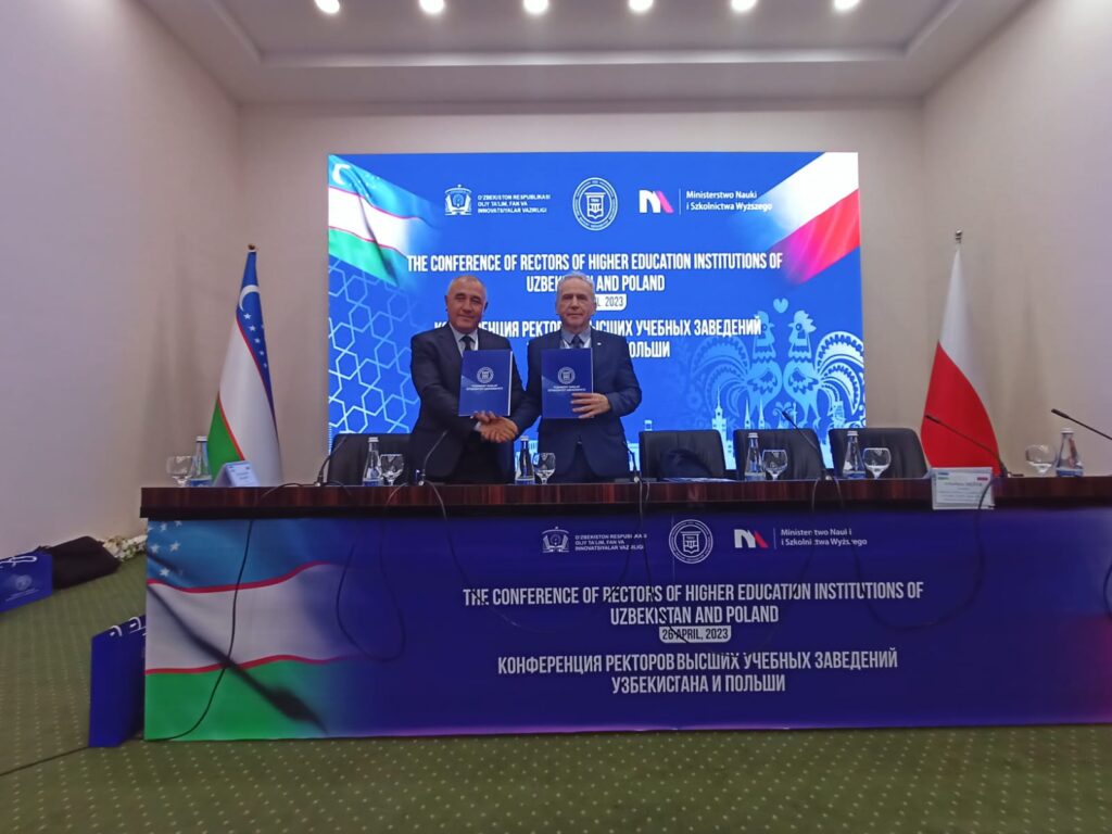 Dwóch mężczyzn podpisuje dokumenty na konferencji rektorów uczelni Uzbekistanu i Polski.