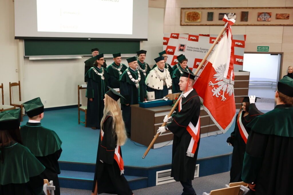 Uroczystość akademicka z udziałem osób w togach i biretach. Kluczowe obiekty: togi, birety, polska flaga.