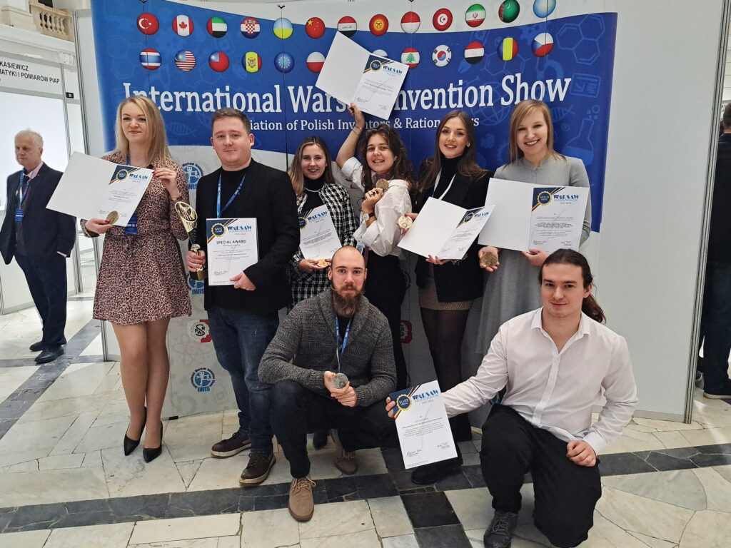 Grupa osób pozuje z dyplomami i medalami na tle banera 