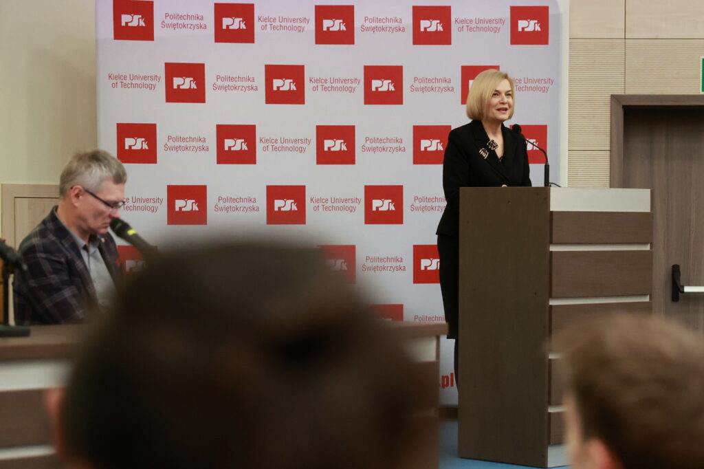 Kobieta przemawia przy mównicy na tle baneru Politechniki Świętokrzyskiej. W tle mężczyzna.