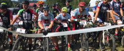 Grupa kolarzy górskich w kaskach i strojach sportowych stoi przy rowerach na starcie zawodów.