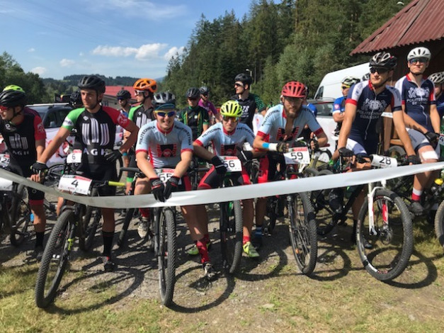 Grupa kolarzy górskich w kaskach i strojach sportowych stoi przy rowerach na starcie zawodów.