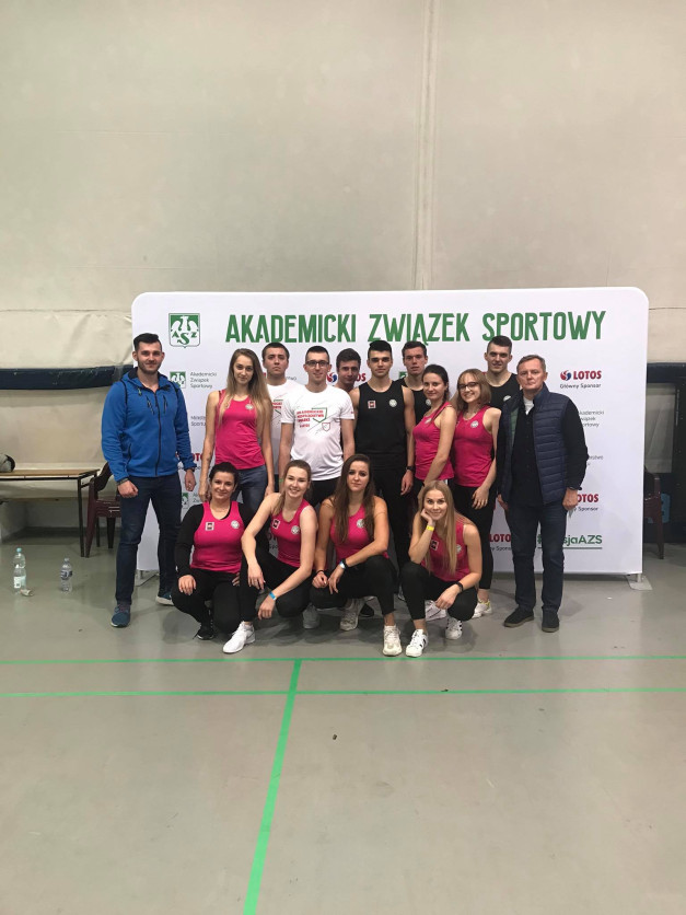 Grupa osób pozuje do zdjęcia przed banerem "Akademicki Związek Sportowy". Kluczowe obiekty: ludzie, baner, logo LOTOS.