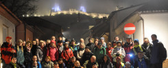 Grupa ludzi pozuje do zdjęcia nocą przed zamkiem. Widać zamek, budynki i znak drogowy.