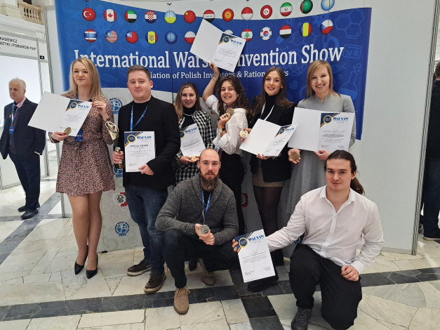 Grupa osób pozuje z dyplomami i medalami na tle banera "International Warsaw Invention Show".