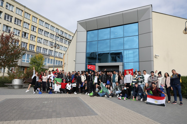 Grupa studentów pozuje do zdjęcia przed budynkiem uczelni. Widać flagi Turcji, Egiptu i Algierii.