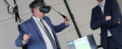 Mężczyzna w goglach VR i garniturze testuje symulator. Obok stoi drugi mężczyzna w garniturze.