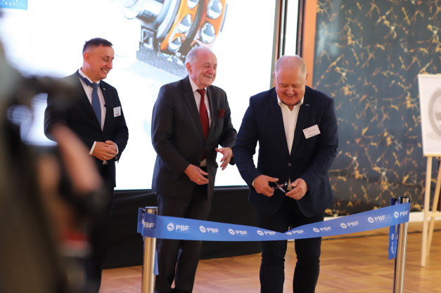 Trzech mężczyzn w garniturach przecina niebieską wstęgę z logo PBF. Kontekst: uroczystość otwarcia.