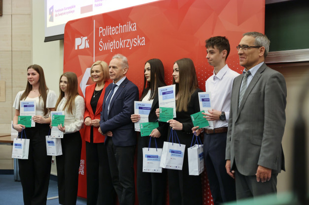 Grupa osób odbiera dyplomy i upominki na tle Politechniki Świętokrzyskiej. Kluczowe obiekty: ludzie, dyplomy, torby.