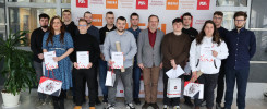 Grupa osób z dyplomami i torbami przed banerem Politechniki Świętokrzyskiej. Kontekst: wydarzenie uczelniane.