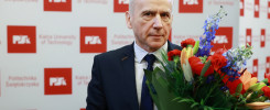 Mężczyzna w garniturze trzyma bukiet kwiatów. Tło to ściana z logo Politechniki Świętokrzyskiej.