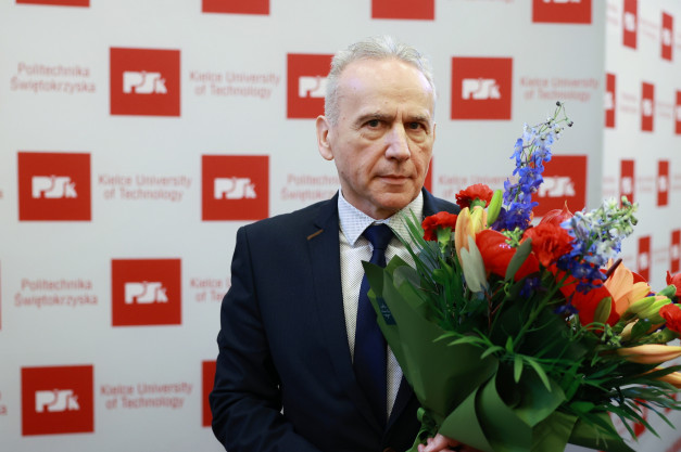 Mężczyzna w garniturze trzyma bukiet kwiatów. Tło to ściana z logo Politechniki Świętokrzyskiej.