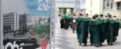 Plakat Politechniki Świętokrzyskiej z budynkami i rokiem 2025. W tle grupa osób w togach.