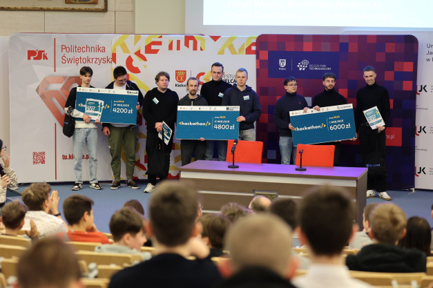 Grupa młodych ludzi odbiera nagrody pieniężne na scenie, podczas wydarzenia typu hackathon.