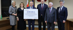 Sześć osób pozuje z czekiem na 8 mln zł dla Politechniki Świętokrzyskiej. Kluczowe obiekty: czek, ludzie, godło Polski.