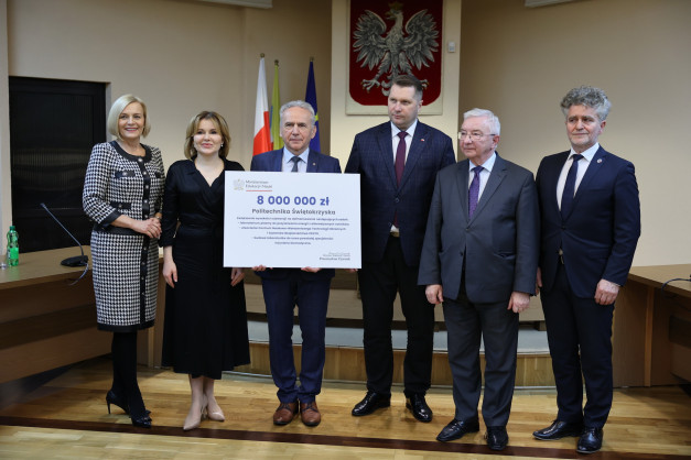 Sześć osób pozuje z czekiem na 8 mln zł dla Politechniki Świętokrzyskiej. Kluczowe obiekty: czek, ludzie, godło Polski.