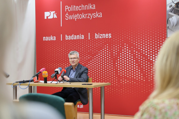 Mężczyzna w okularach siedzi przy stole z mikrofonami. Kontekst: konferencja prasowa Politechniki Świętokrzyskiej.