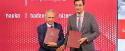 Dwóch mężczyzn w garniturach trzyma dokumenty. Tło to czerwona ściana z napisem "Politechnika Świętokrzyska".