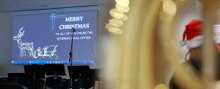 Ekran z napisem "Merry Christmas" i reniferem. W tle widać krzesła i mikrofon. Kontekst: wydarzenie świąteczne.