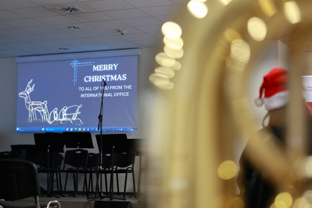 Ekran z napisem "Merry Christmas" i reniferem. W tle widać krzesła i mikrofon. Kontekst: wydarzenie świąteczne.