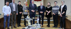 Grupa osób pozuje obok łazika marsjańskiego. W tle godło Polski i flagi.