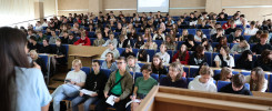 Wykład w auli uniwersyteckiej. Studenci siedzą w ławkach, słuchając wykładowcy. W tle ekran projekcyjny.