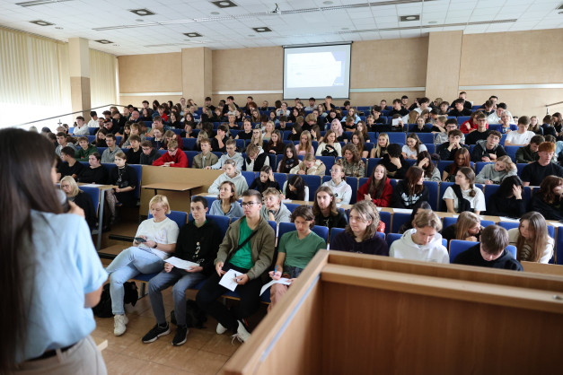 Wykład w auli uniwersyteckiej. Studenci siedzą w ławkach, słuchając wykładowcy. W tle ekran projekcyjny.