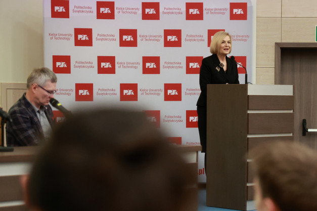 Kobieta przemawia przy mównicy na tle baneru Politechniki Świętokrzyskiej. W tle mężczyzna.