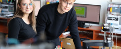 Dwoje studentów w okularach pracuje przy robocie. W tle komputery i sprzęt laboratoryjny.