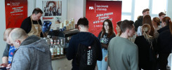 Ludzie stoją przy stoisku z kawą, na tle banerów promujących program Erasmus+.