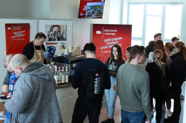 Ludzie stoją przy stoisku z kawą, na tle banerów promujących program Erasmus+.