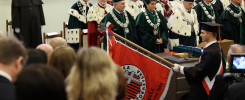 Uroczystość akademicka z udziałem osób w togach. Widoczny sztandar z napisem "Kielce Rok Założenia 1965".