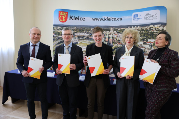 Pięć osób w garniturach trzyma dokumenty przed banerem z napisem "CK Kielce".