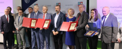 Grupa osób w garniturach odbiera nagrody. W tle baner Urzędu Marszałkowskiego Województwa Świętokrzyskiego.