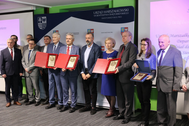 Grupa osób w garniturach odbiera nagrody. W tle baner Urzędu Marszałkowskiego Województwa Świętokrzyskiego.