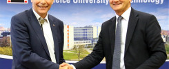 Dwóch mężczyzn w garniturach ściska sobie dłonie. W tle logo Politechniki Opolskiej i budynek uniwersytecki.