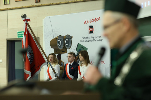 Flaga Polski i trzech studentów w szarfach. Tło: Politechnika Świętokrzyska. Kontekst: uroczystość.