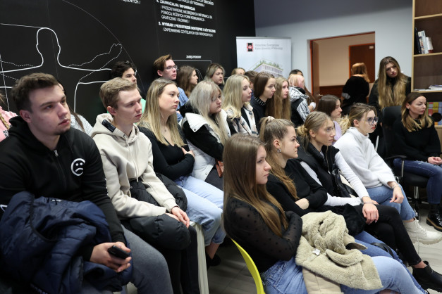 Grupa młodych ludzi siedzi na krzesłach, słuchając. W tle widać tablicę z rysunkiem ludzkiej sylwetki.