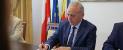 Mężczyzna w garniturze podpisuje dokument. W tle flagi Polski, UE i Ukrainy.